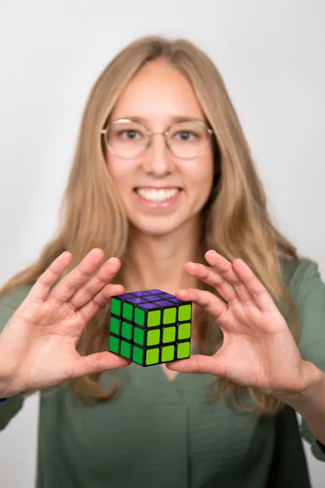 DEBATIN_Produktsparten_Headerbild_DEBADEINS_Simonis_RubikWürfel Sina Simonis porte un chemisier vert et tient un Rubik’s Cube aux couleurs de DEBATIN.