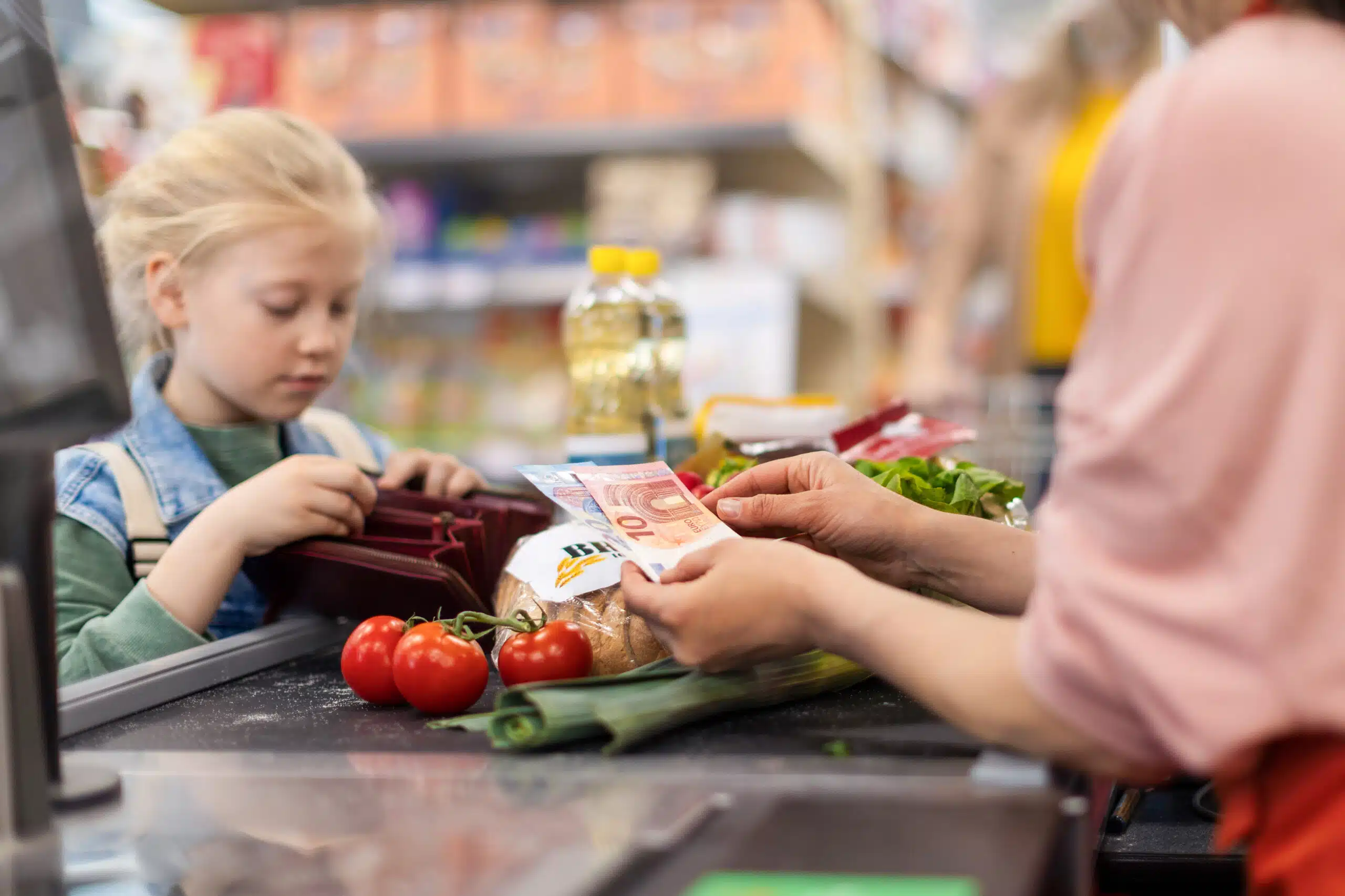 Close-up of little blond girl paying for grocery shopping in supermarket. Gros plan sur une petite fille blonde qui paye ses courses au supermarché.