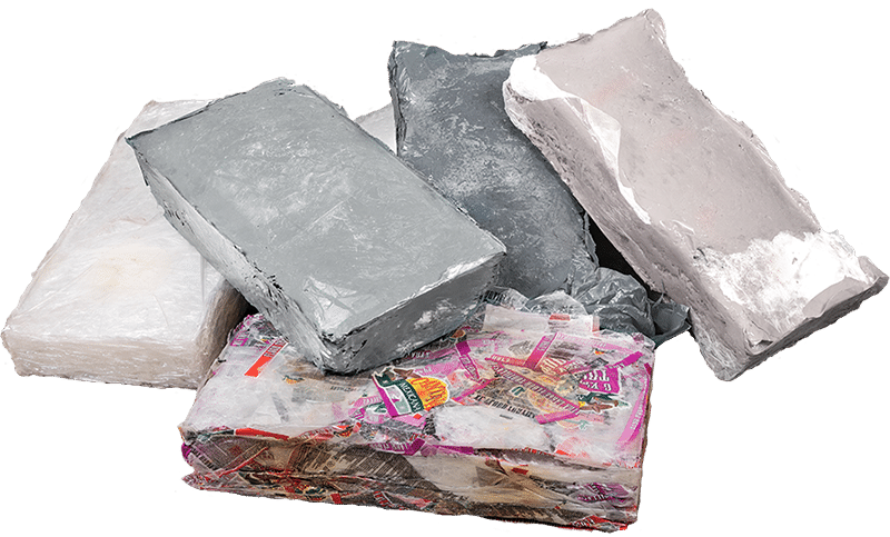 Une vue rapprochée de plusieurs blocs solides de films plastiques thermoformés et fusionnés, de forme irrégulière, montrant la forme compacte du matériau recyclé après son traitement par une presse à balles thermiques.