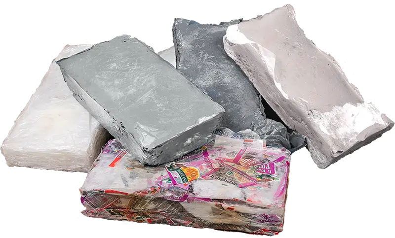 Gepresste Kunstofftaschen Une vue rapprochée de plusieurs blocs solides de films plastiques thermoformés et fusionnés, de forme irrégulière, montrant la forme compacte du matériau recyclé après son traitement par une presse à balles thermiques.