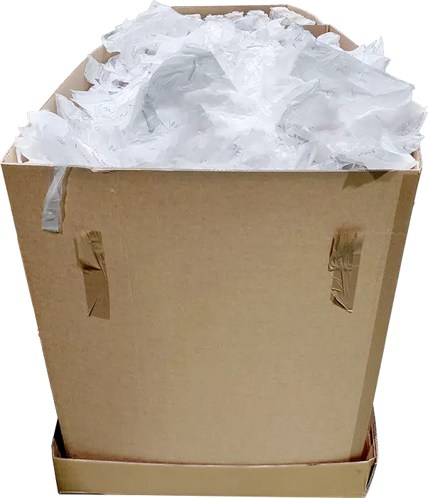 Gesammelte Kunststofftaschen in Karton Un carton débordant de pochettes plastiques blanches en vrac et froissées, illustrant l’état initial des déchets plastiques collectés avant le compactage.