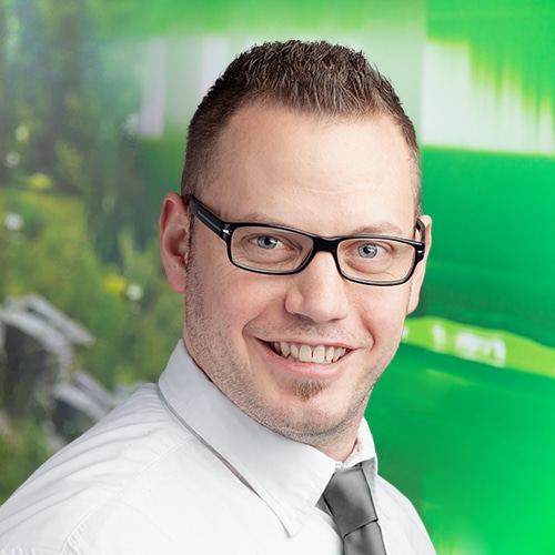 Portrait de Florian Klonig, Responsable du Département Expédition chez Debatin. Son large sourire et ses lunettes distinctives marquent son visage, encadré de cheveux foncés courts et d’une barbe soignée.