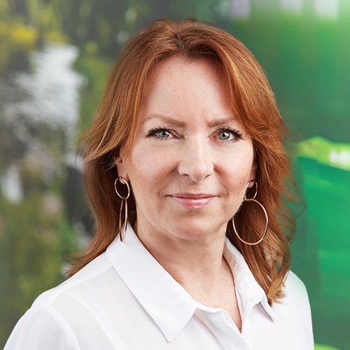 Portrait de Francoise Mathieu, Support commercial chez Debatin. Elle sourit doucement à la caméra, a des cheveux brun-roux et de grandes boucles d’oreilles dorées.