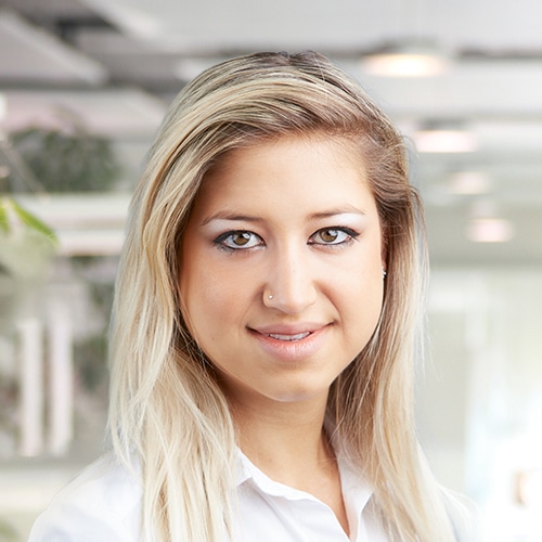 Gros plan de Jennifer Petko, Département Expédition chez Debatin. Son sourire ouvert et ses longs cheveux blonds se distinguent. Elle porte un chemisier blanc classique soulignant son professionnalisme.