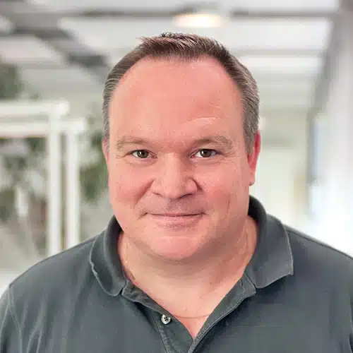 Portrait de Laurent Roser, un homme aux cheveux courts foncés et au regard amical. Il porte un polo sombre. Laurent Roser travaille en Gestion de production chez DEBATIN.