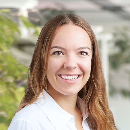 Gros plan de Patricia Polzer, travaillant comme Consultante commerciale / Service client chez Debatin. Une femme souriante avec de longs cheveux bruns portant un chemisier blanc. L’arrière-plan flou montre des tons clairs et verts, suggérant un environnement de bureau.
