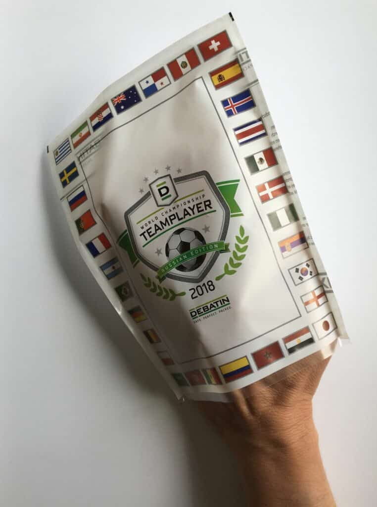 Cleanfix_Hand-1 Main tenant un sachet CLEANFIX® édition Teamplayer Coupe du Monde 2018, décoré de drapeaux et d’un emblème de football.