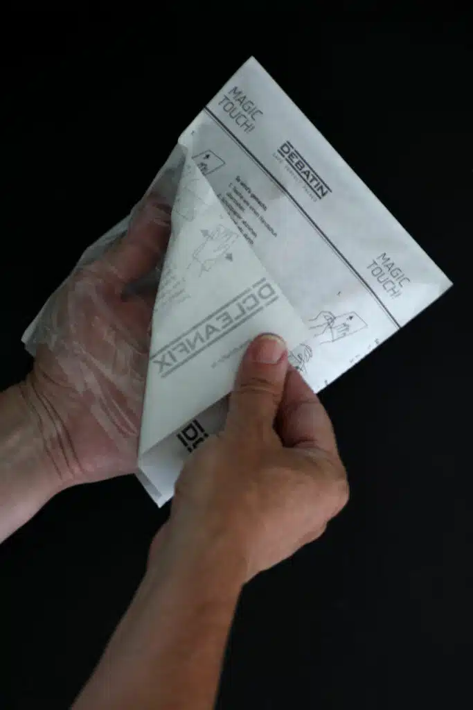 cleanfix_use Mains retirant le papier de protection d’un sachet CLEANFIX®, avec instructions d’utilisation et mention « Magic Touch! ».